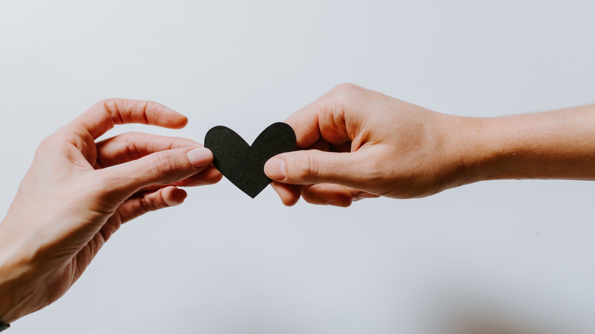 Two hands holding a black paper heart in front of a white background.