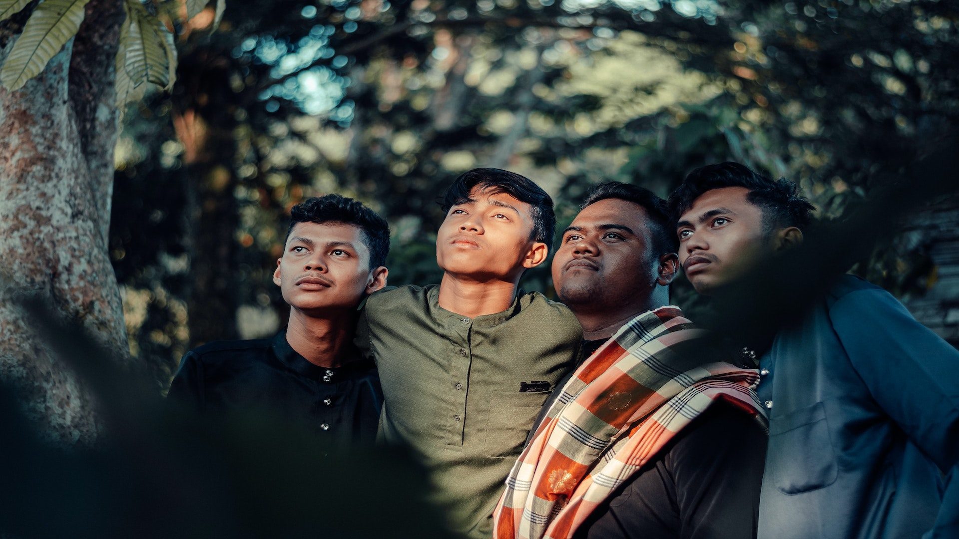 Four Malaysian men next to one another outside in a garden with trees.