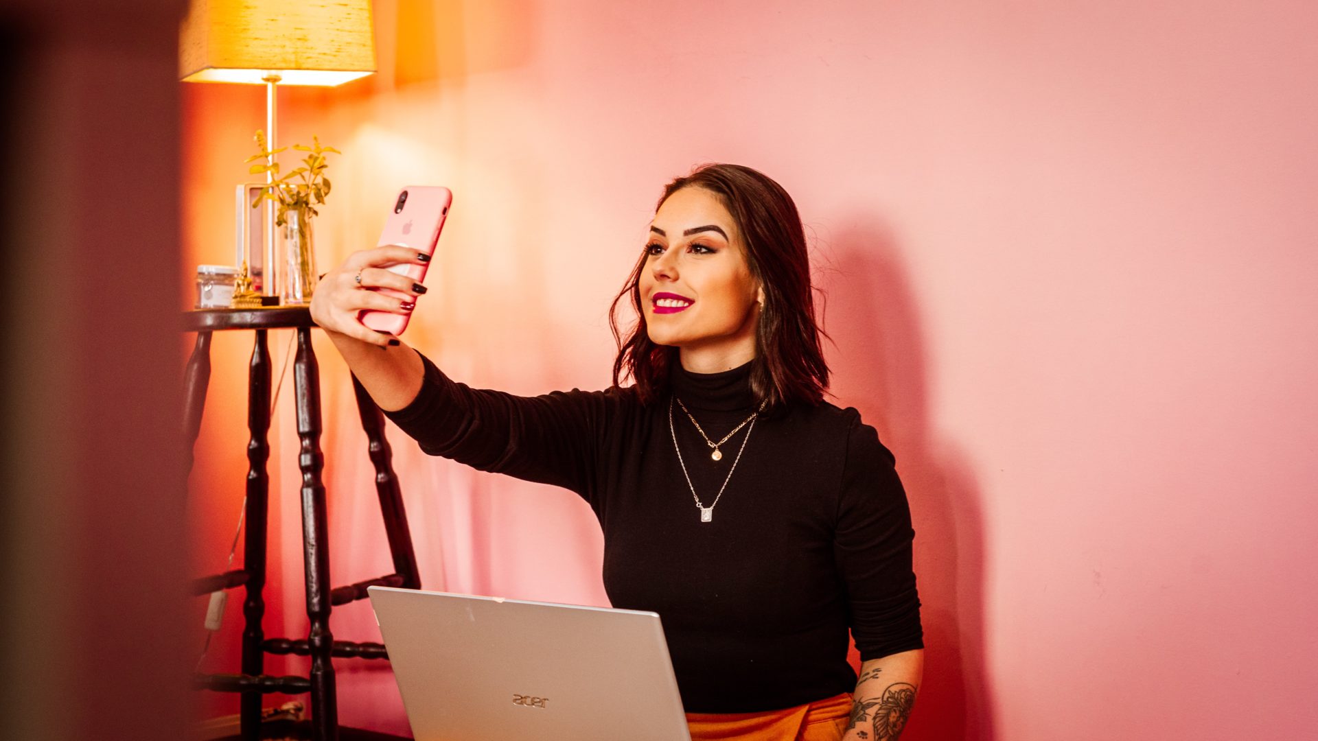 A women in a black long sleeve shirt is holding her pink phone out to take a picture of herself.