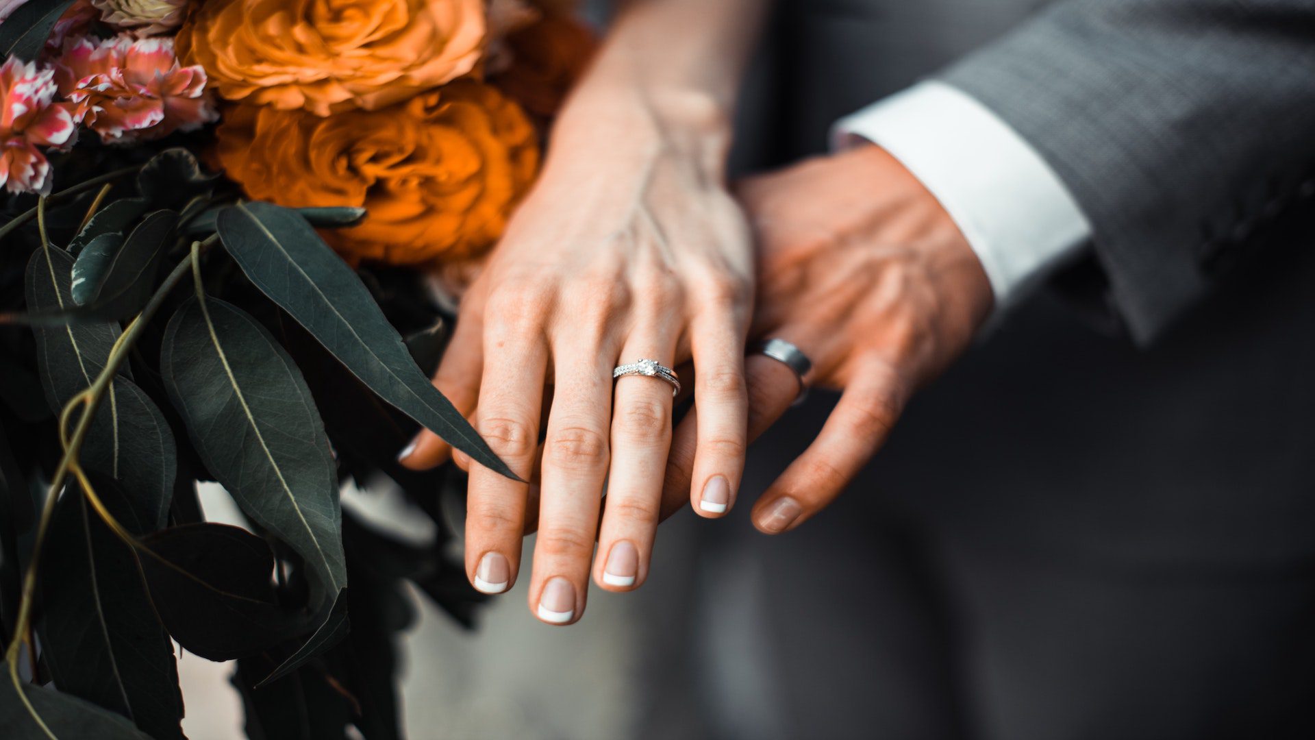 Woman with a boquet of flowers and a man holding out their hands with wedding rings.