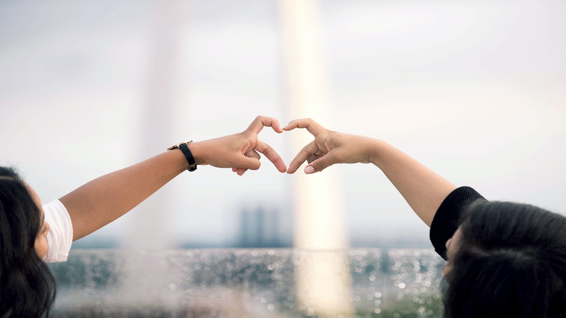 Two women with dark hair forming a heart with their hands.