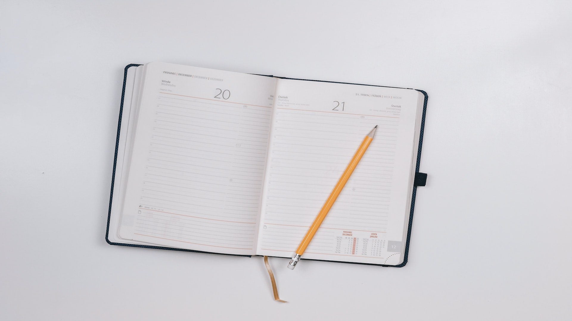 A pencil on an open planner on a white table.