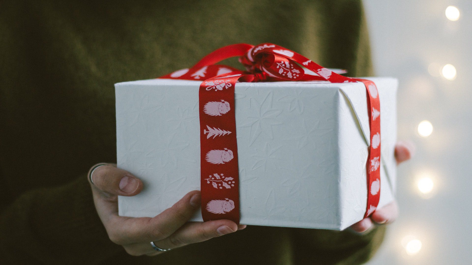 A woman in a green sweater holding a Christmas present wrapped in white wrapping paper and red ribbon.