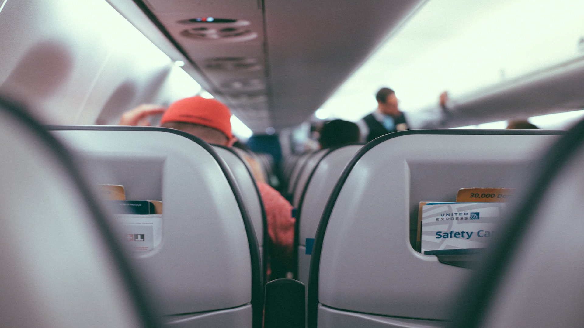 The backs of people sitting in gray airplane seats.