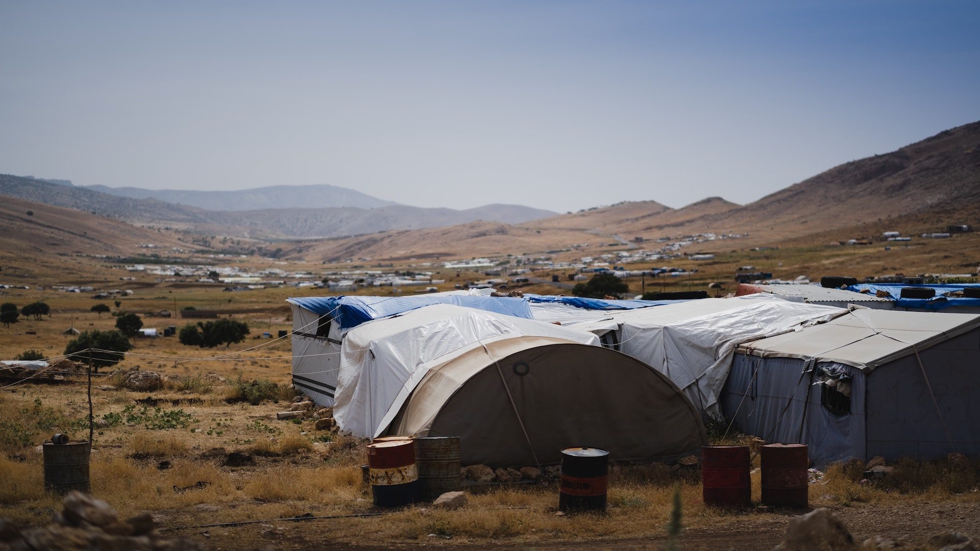 White tents on a brown field surrounded by mountains.