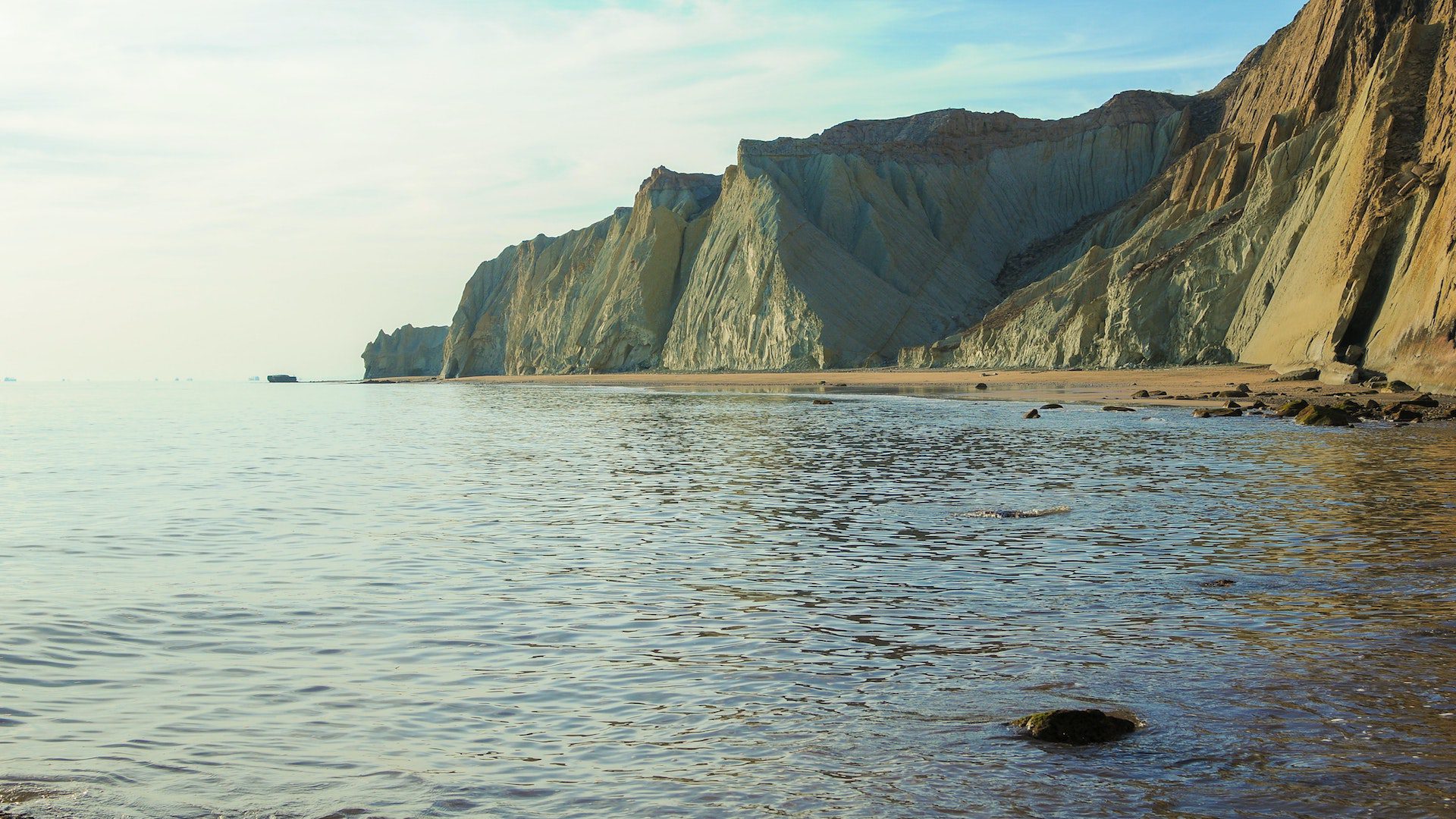 Body of water next to brown, rocky cliffs and a sandy shore.