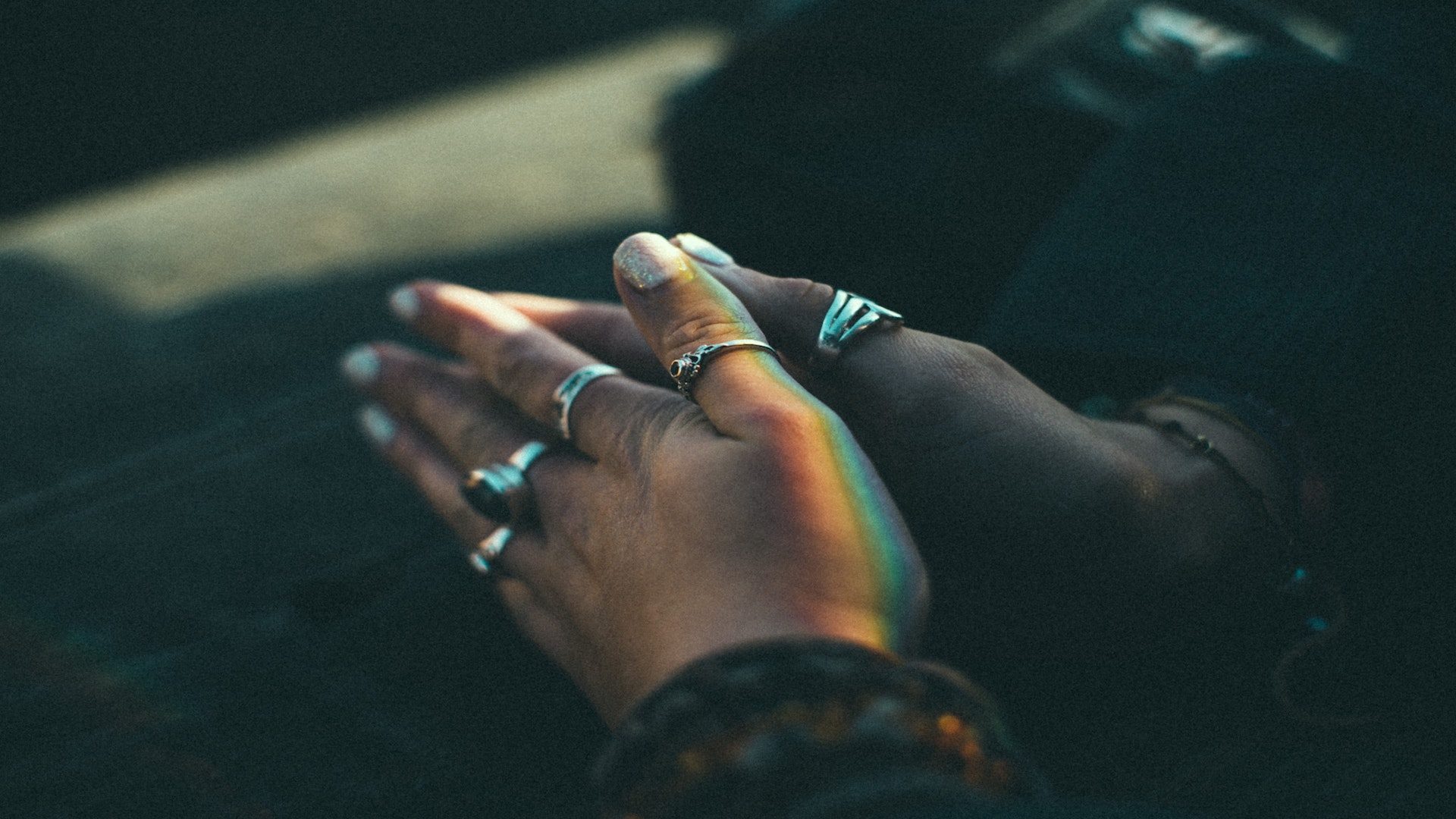 A woman holding her hands with rings and glitter painted fingernails together.
