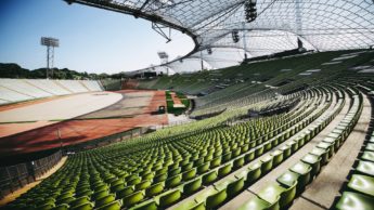Green benches in a stadium covered by a net around a field.