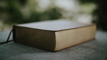 A brown Bible on top of a black table outside.