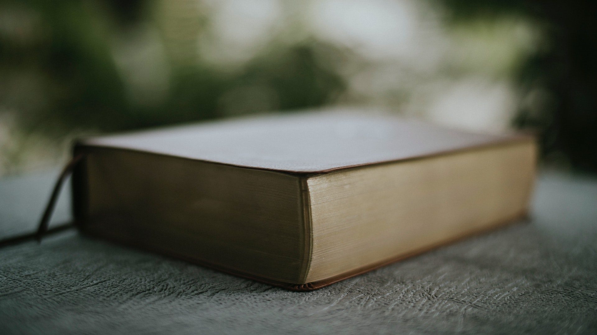 A brown Bible on top of a black table outside.