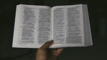 A hand holding an open Bible in front of a black background.