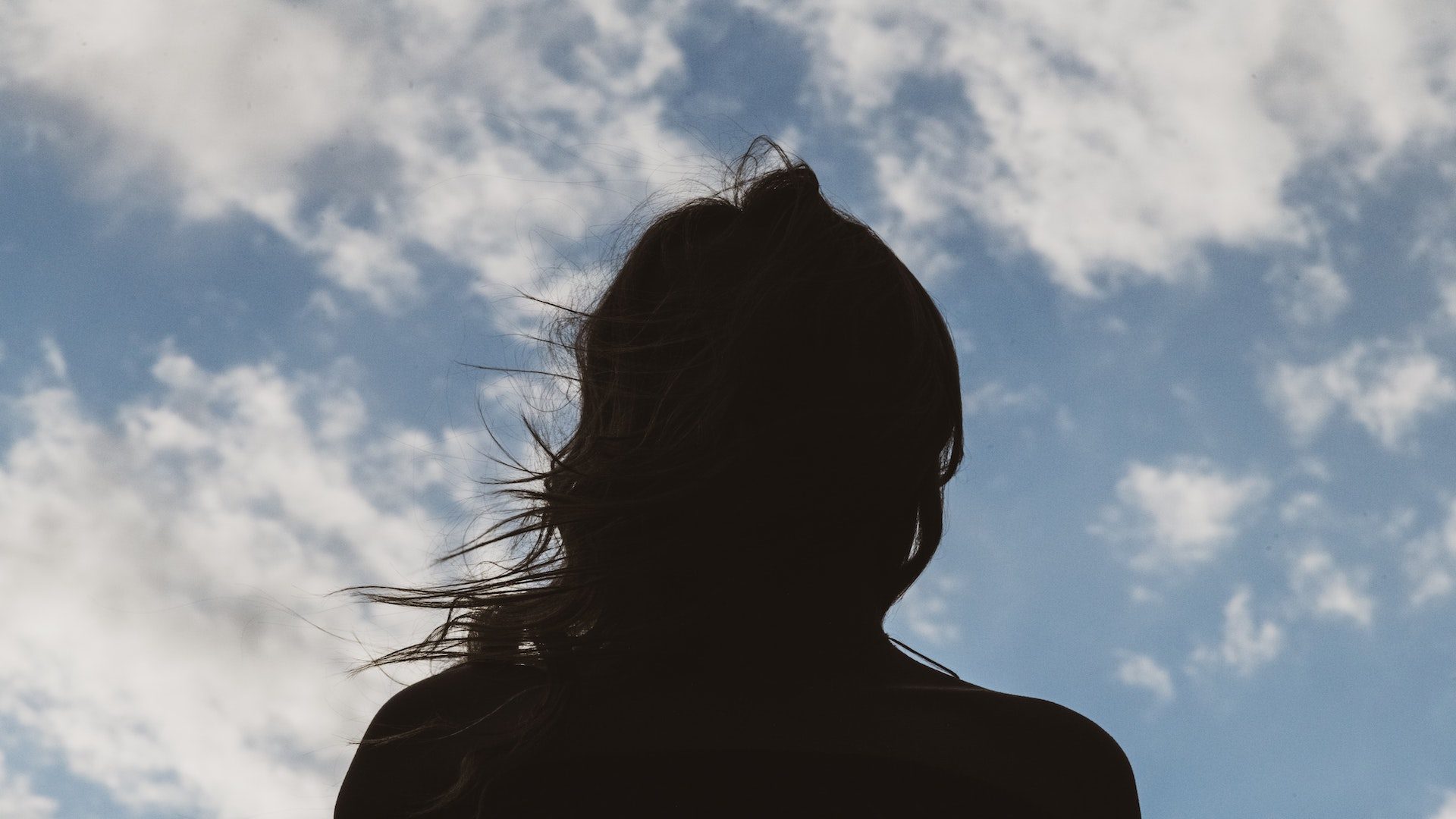 Silhouette of a woman in front of a blue sky and clouds.
