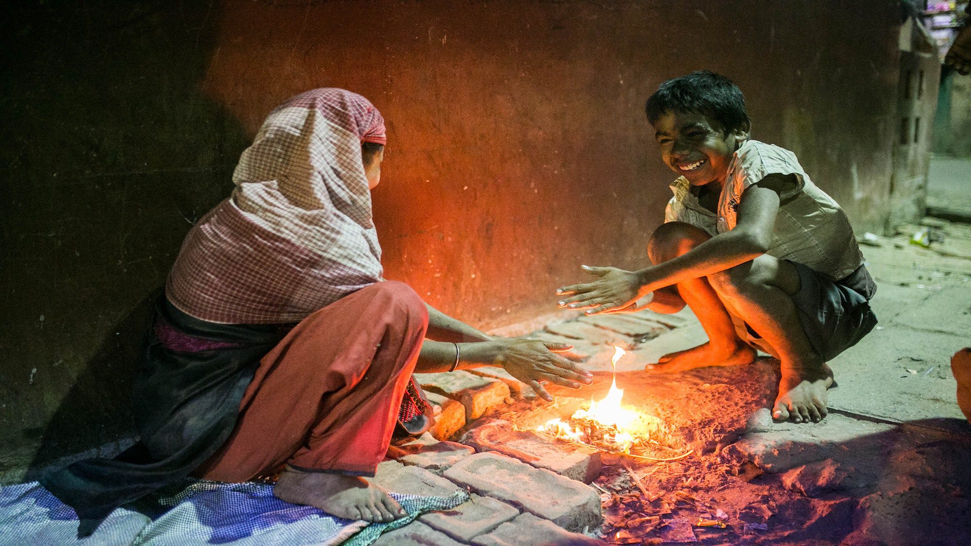 An Indian woman and boy sitting on a brick ground in front of a fire.