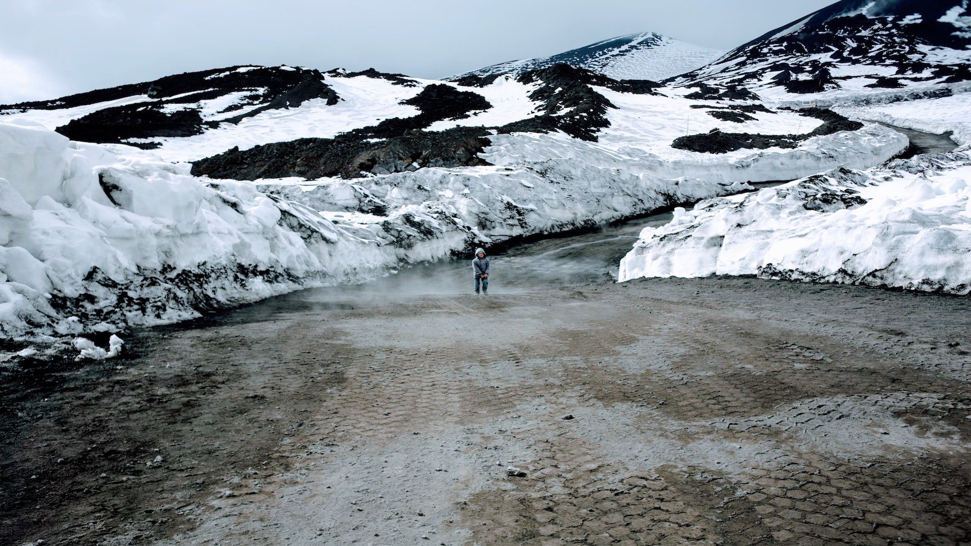 A person standing on a path in between black snow covered mountains.