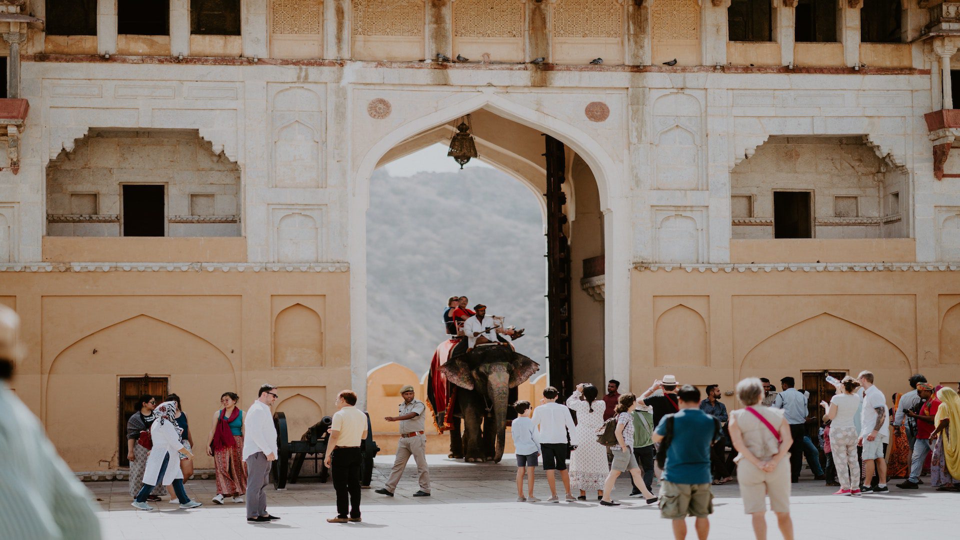 People riding an elephant and people standing in front of a brown Hindu temple.