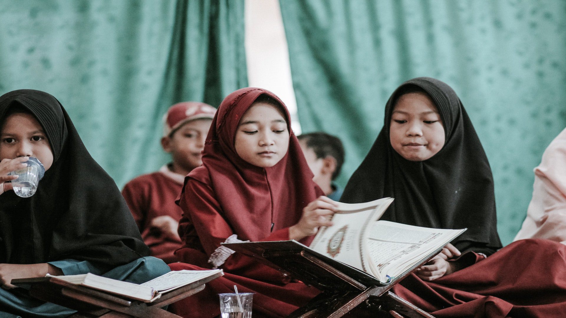 Young muslim girls in hijabs sitting and reading.