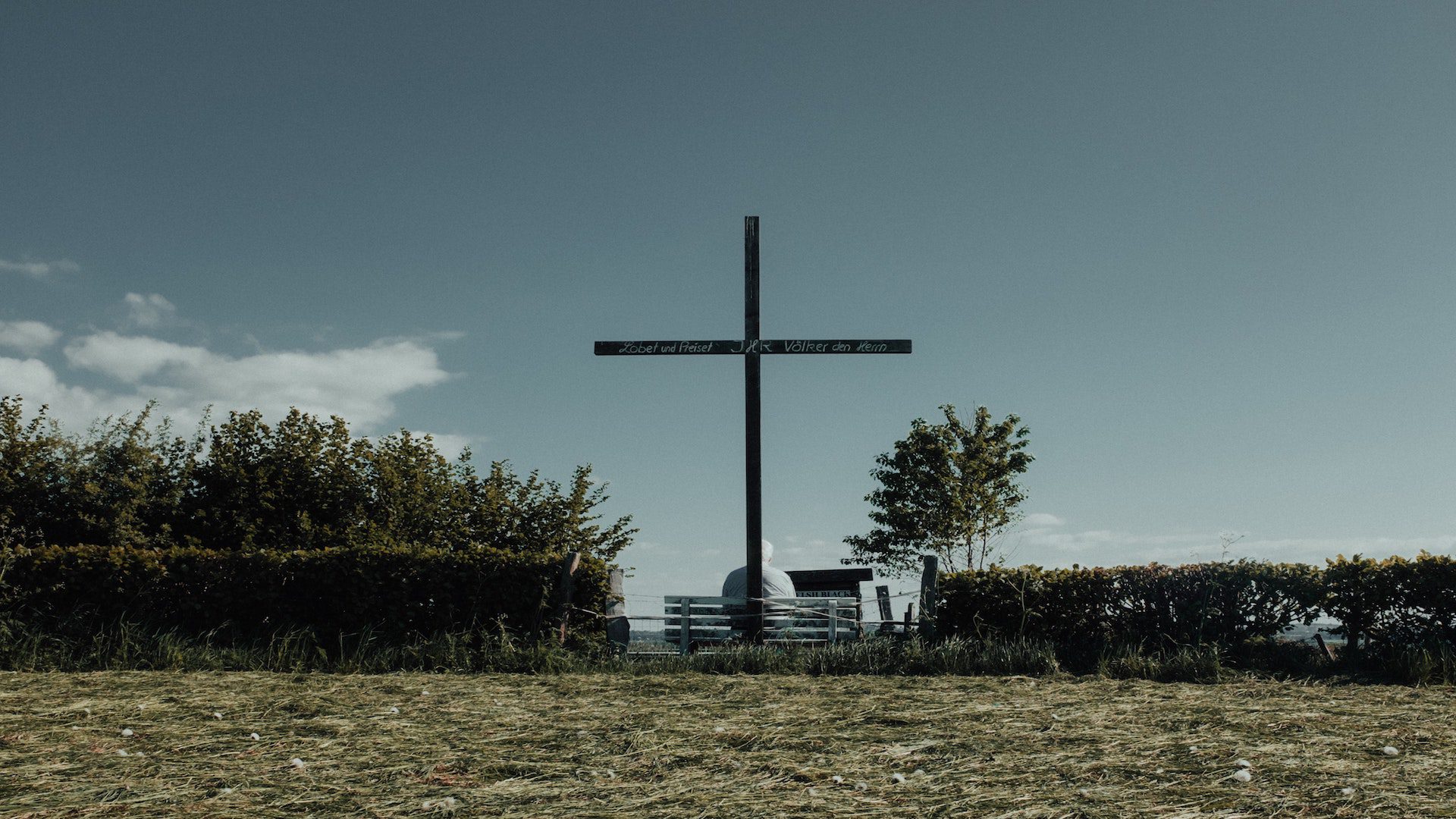 Cross in a grass field lined with shrubs and trees.