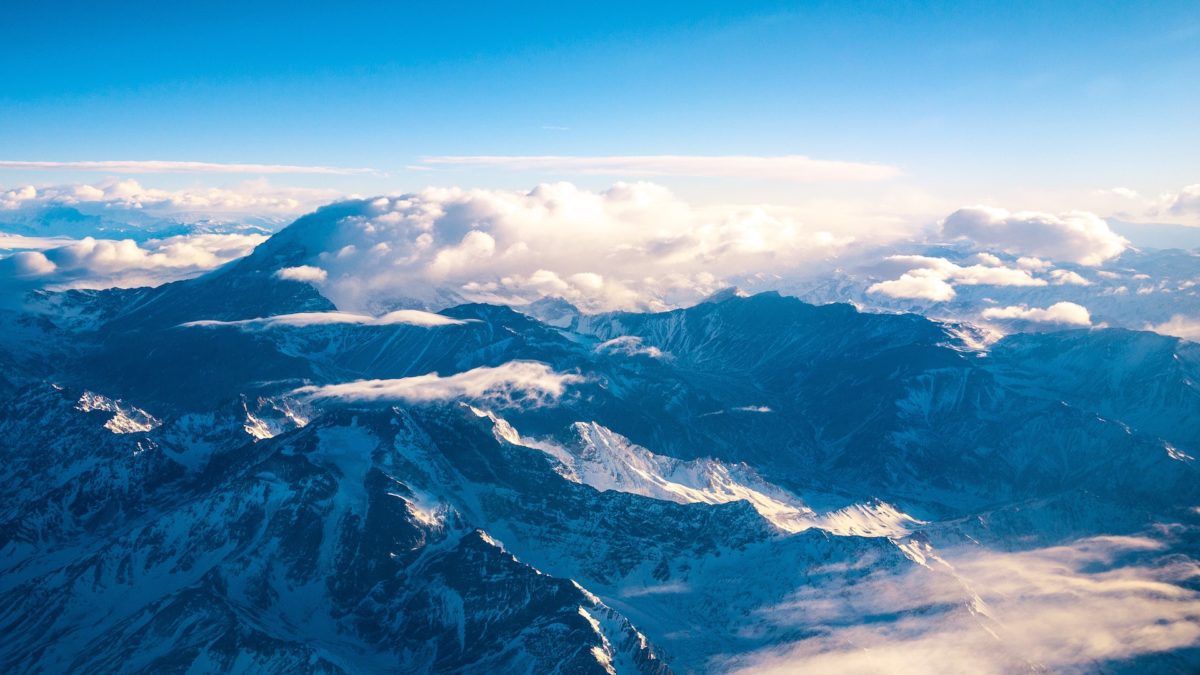 Snow covered mountains covered in clouds and a blue sky.