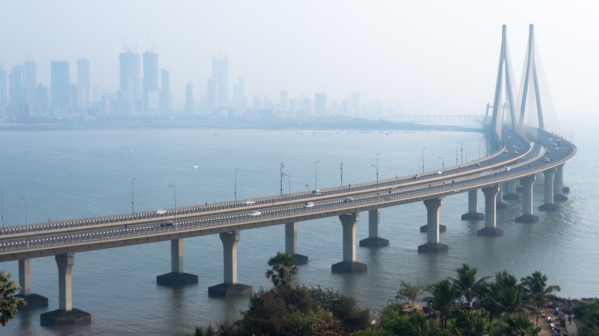 A bridge with cars over water with a city skyline in the background.