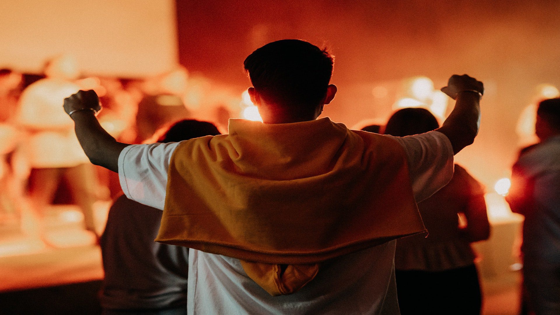 Back of a man in a white shirt and orange sweatshirt with his arms raised.