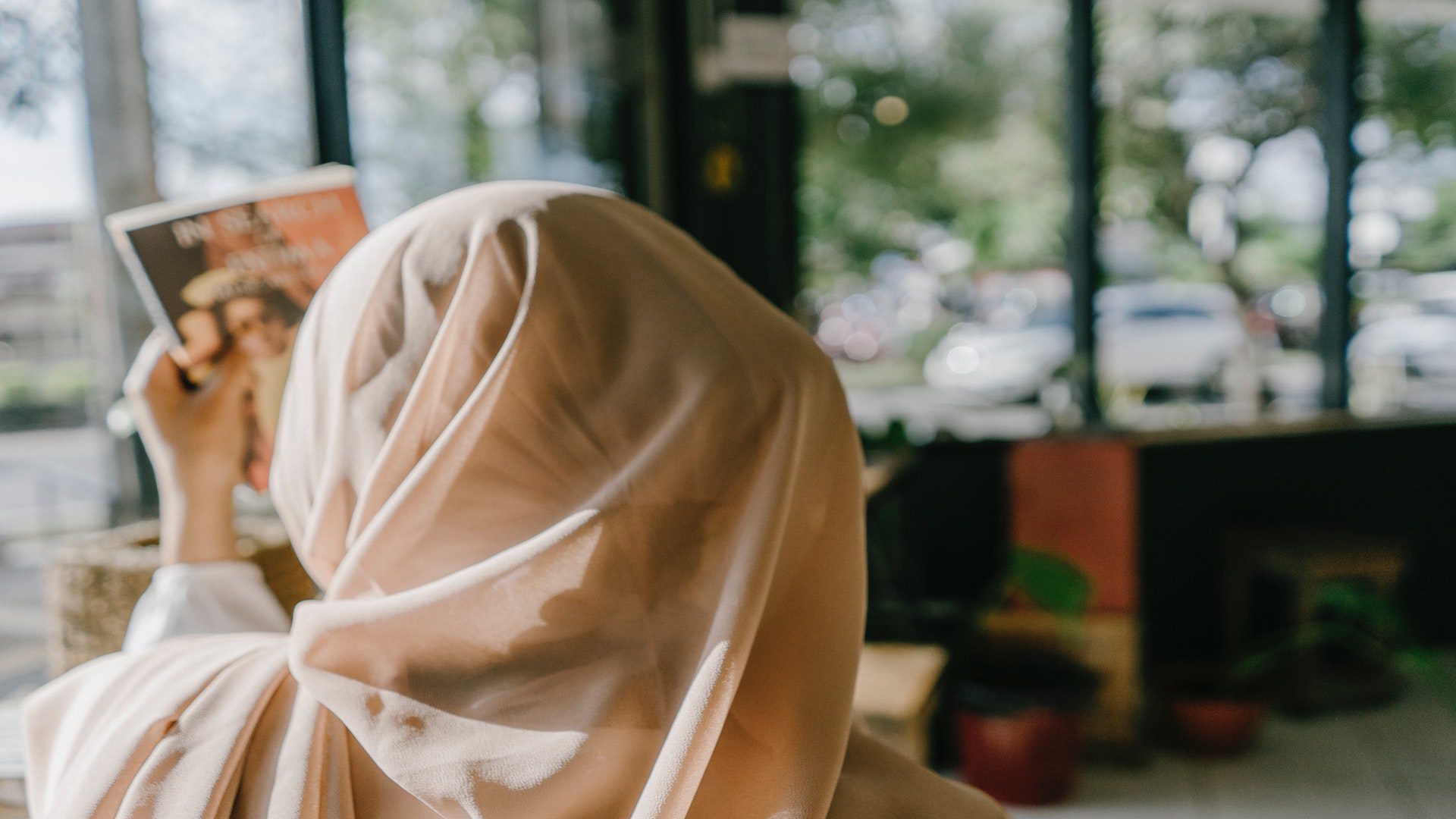 The back of a woman in a tan hijab holding a paper in a store.
