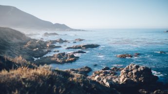 Mountains and rocks next to an ocean on a sunny day.