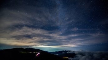 Blue, starry sky over silhouettes of mountains.