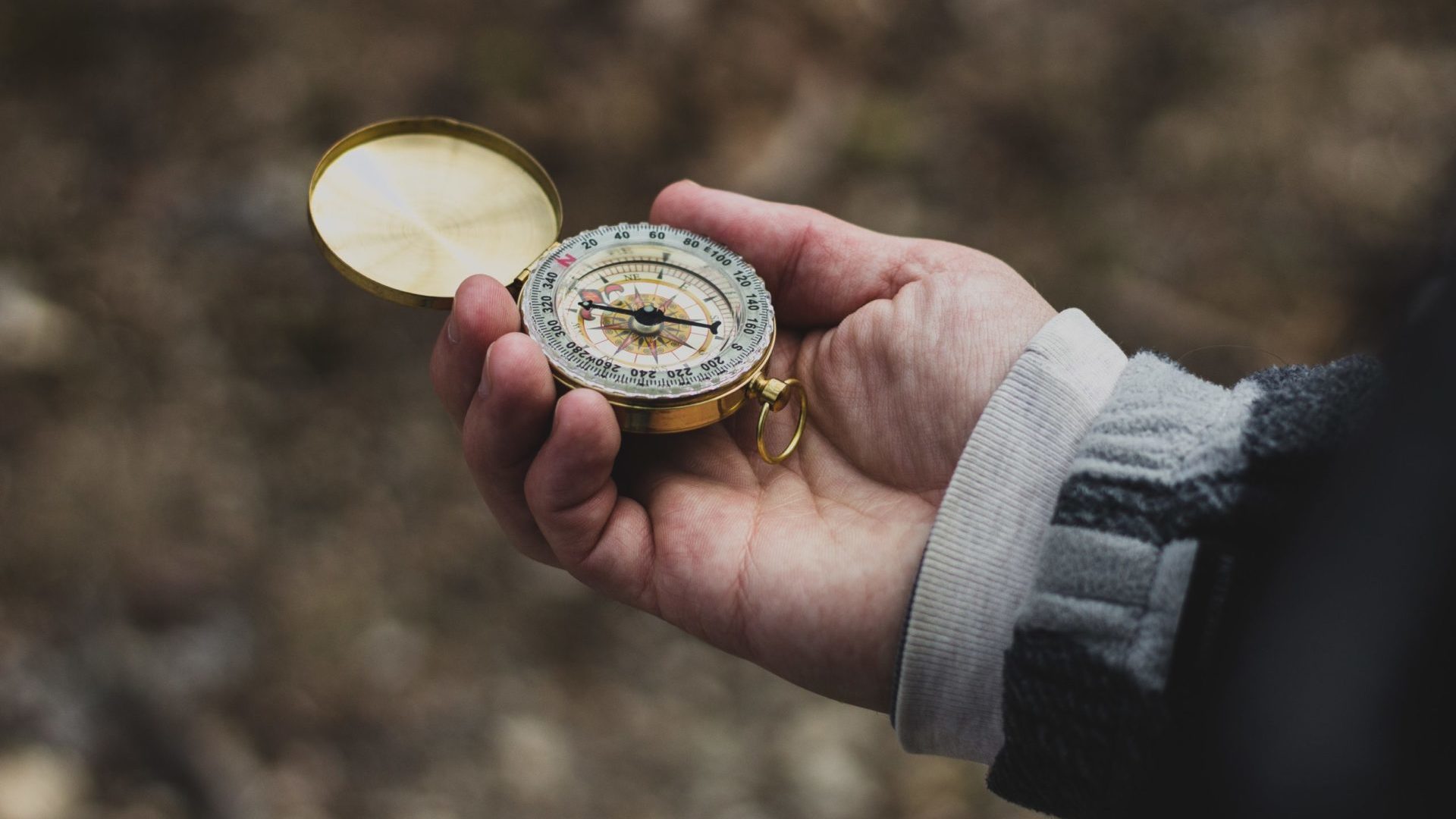 A person is holding a gold compass in their hand.
