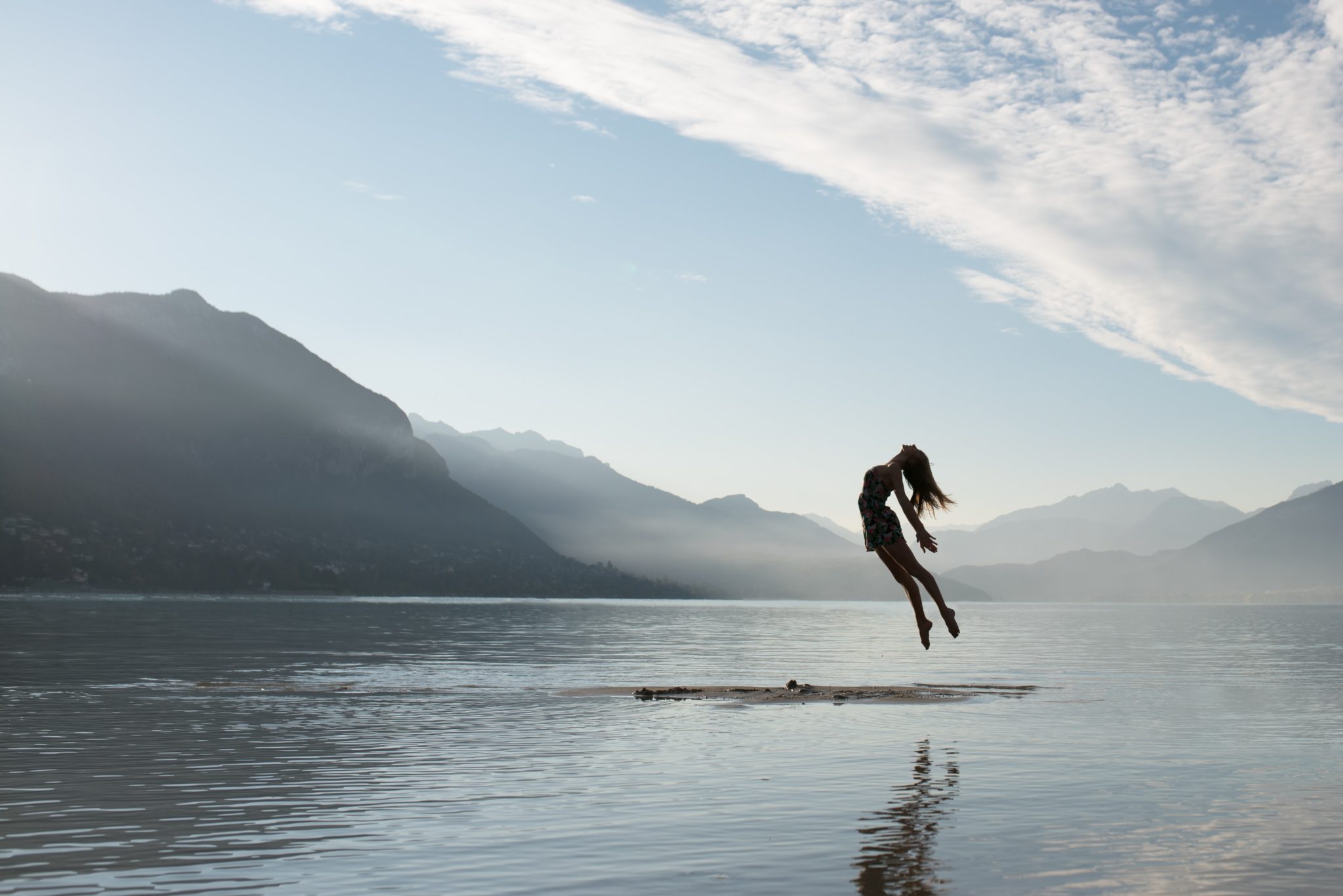 A silhouette of a woman jumping and arching her back in the middle of a lake.