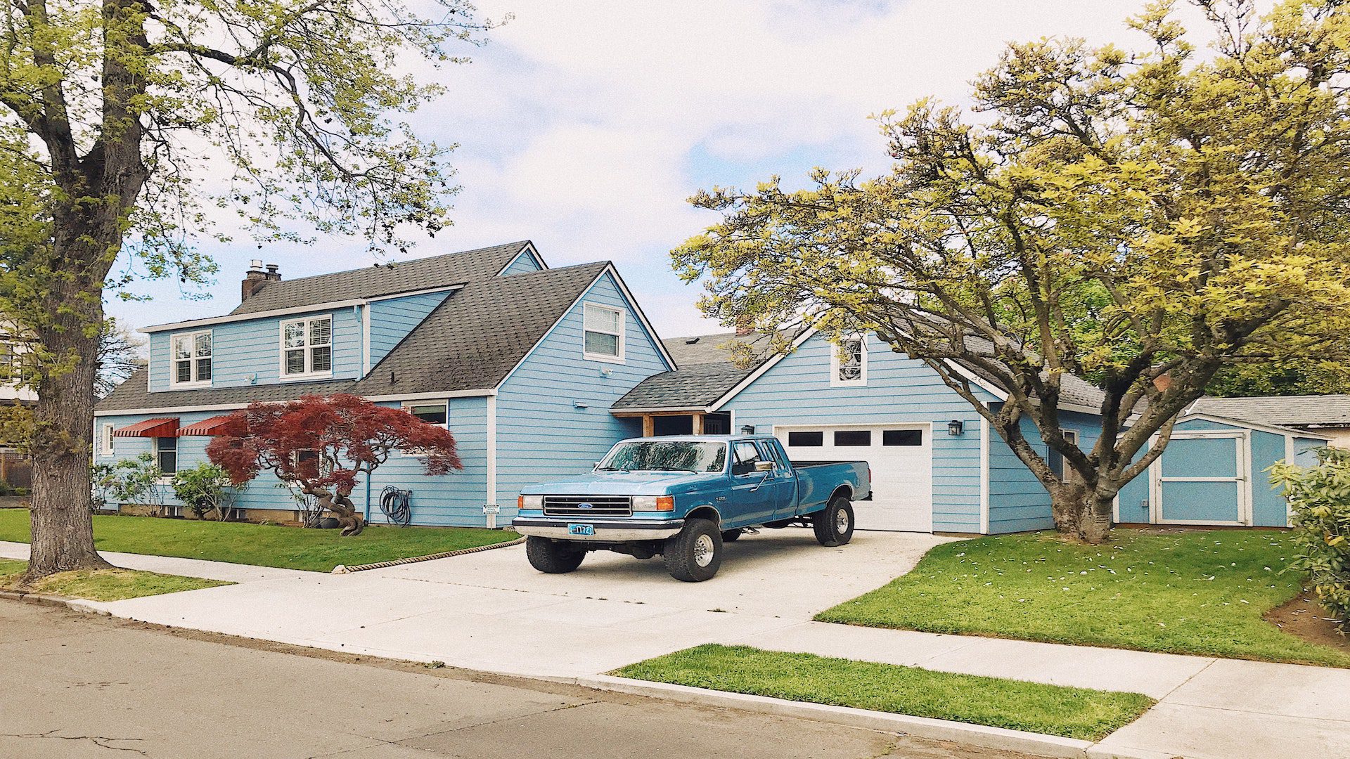A blue Ford truck is sitting in the driveway of a two-story blue and white house.