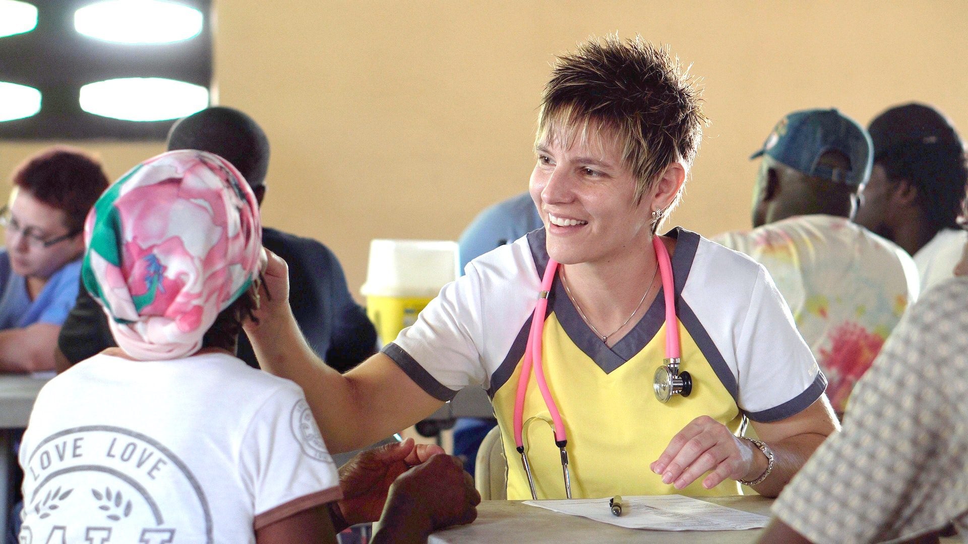 A doctor with a pink stethoscope around her neck is administering aid to a child.