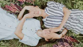 Two girls laying down on the grass, covering their face with their hands.