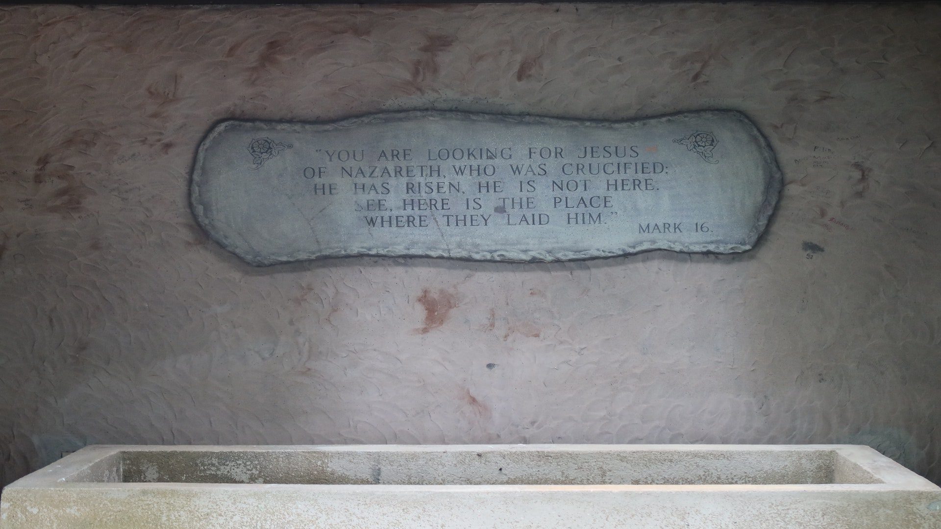 An empty tomb with a carved inscription above it that quotes Mark 16.