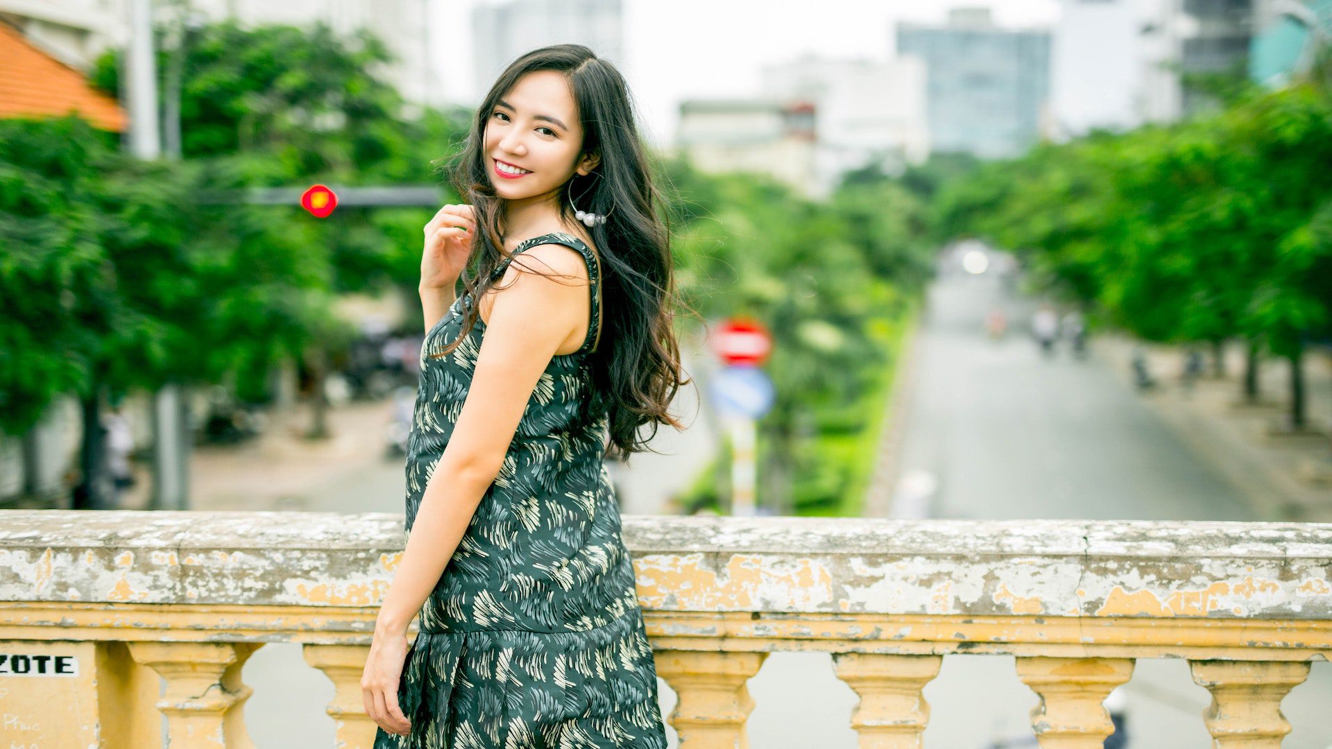 A woman wearing a green sleeveless dress is looking back at the camera while standing on a bridge.