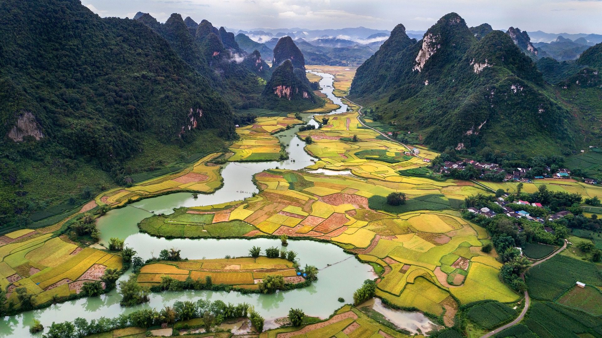 An overhead shot of a lush green valley in Vietnam with a winding river running through the middle.