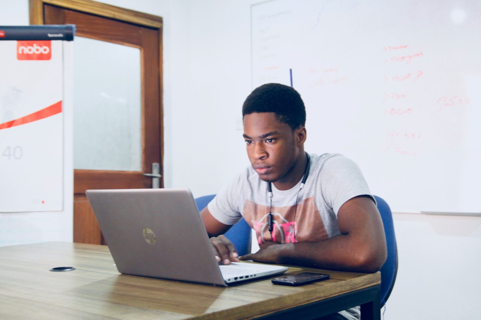 Man sits in a blue chair in front of a computer in an empty classroom.