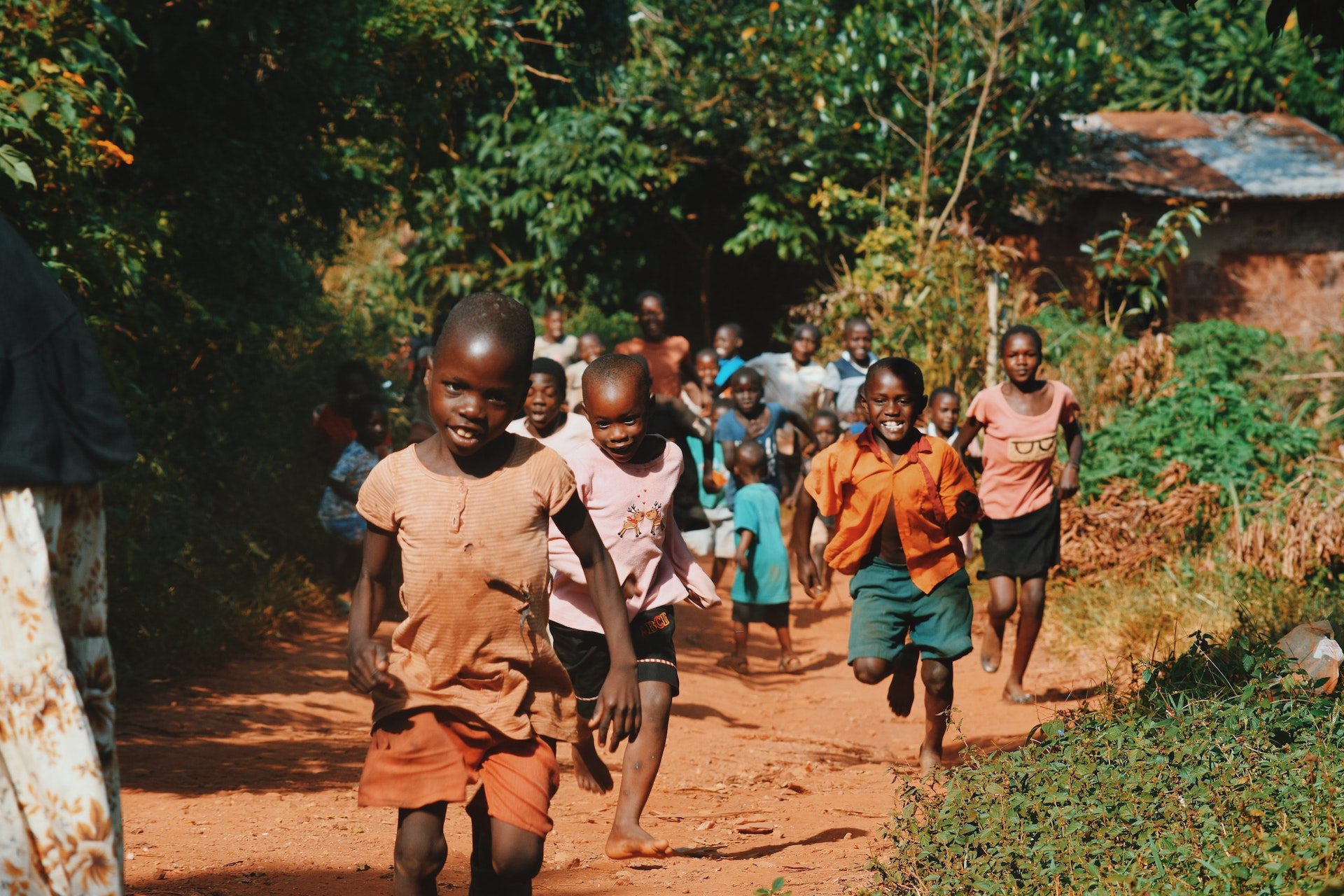 African children run up a dirt path in a wooded area.