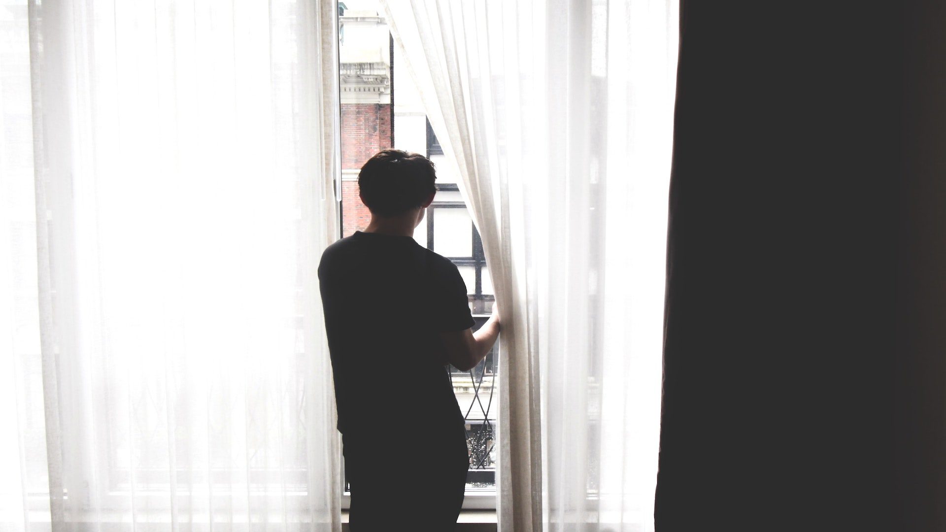 A man is standing next to a window and looking out on the street.