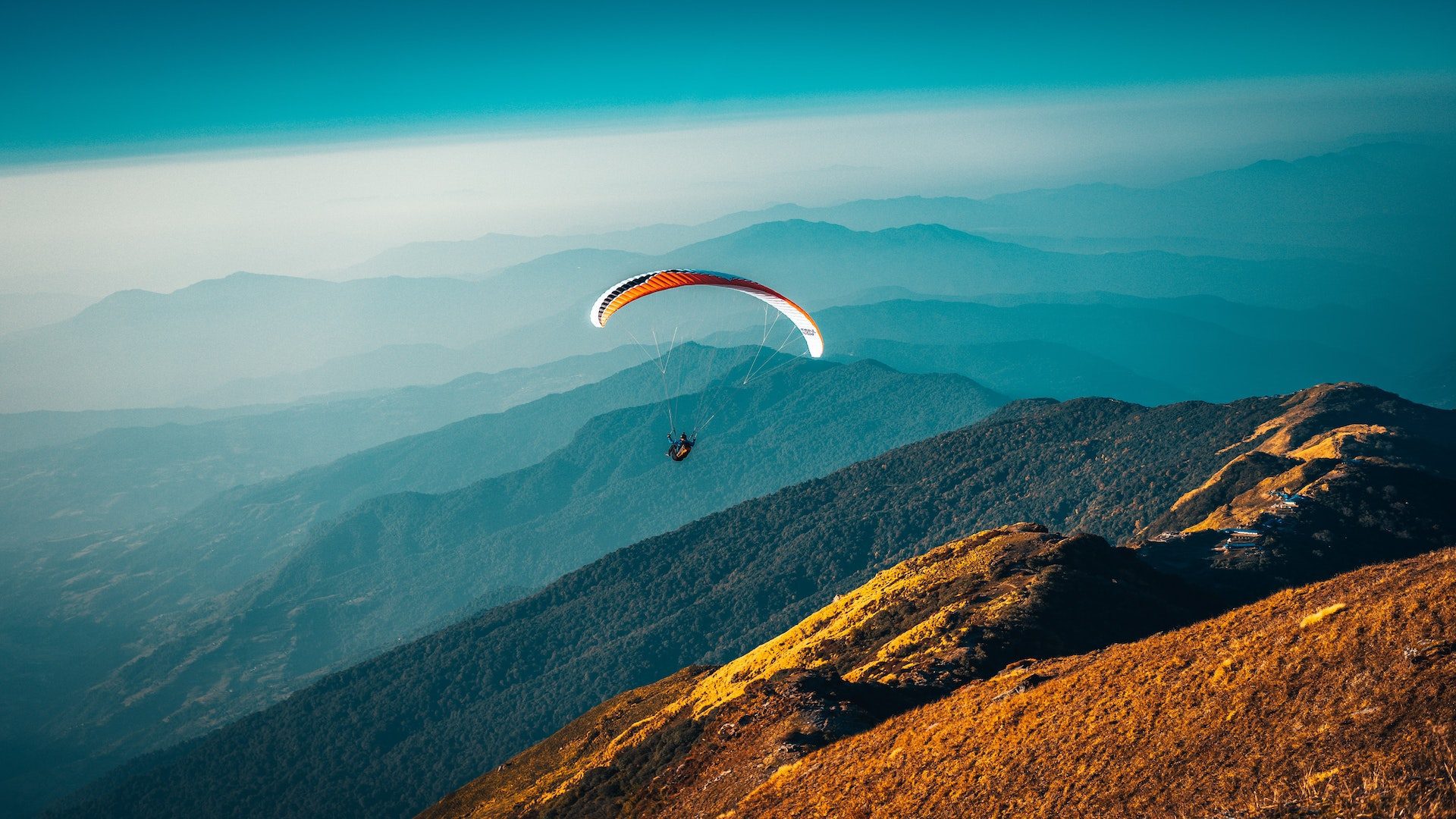 A person is parachuting over the mountains during the daytime.