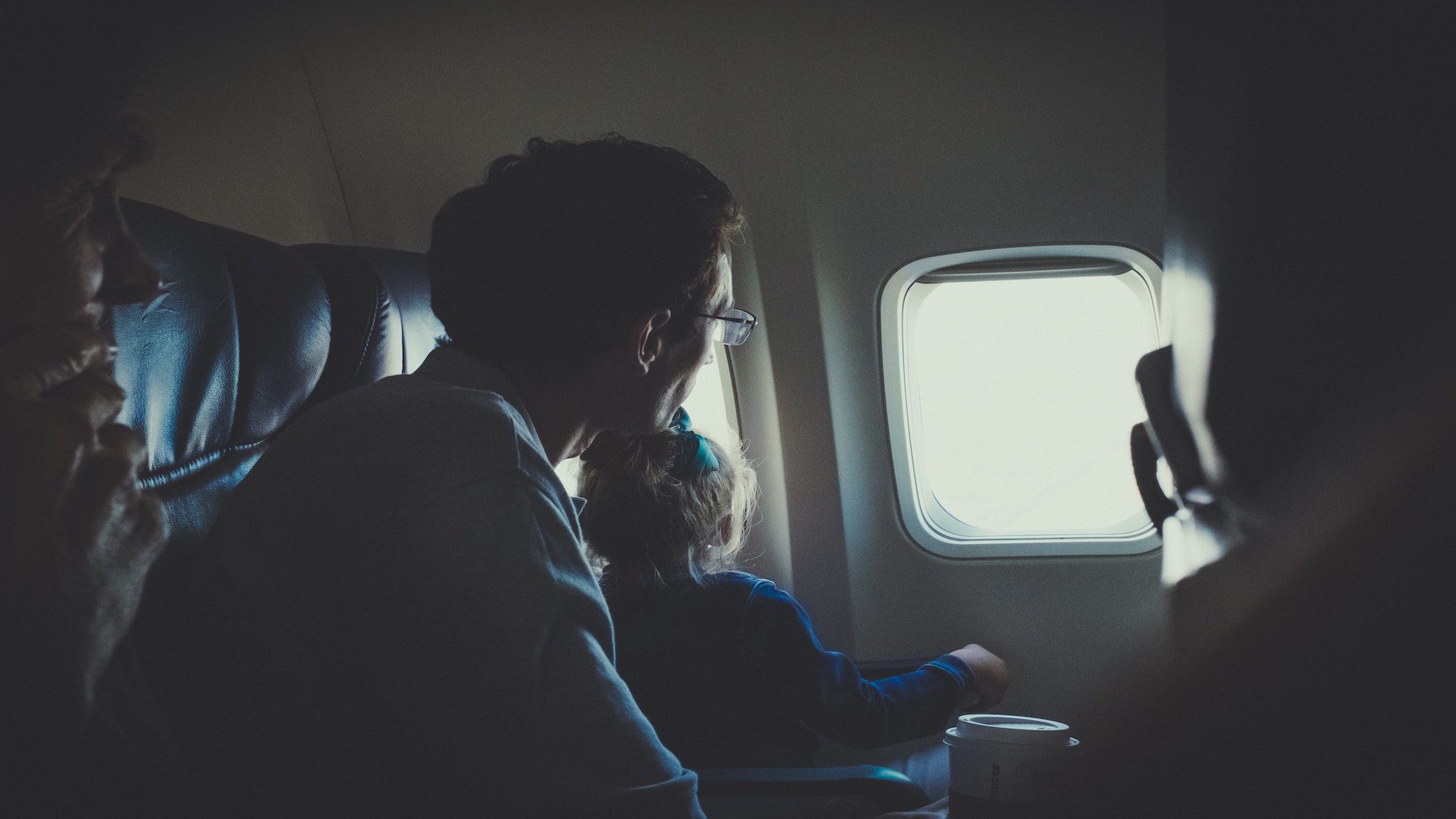 A man and a girl are sitting inside an airplane lookig out the window.