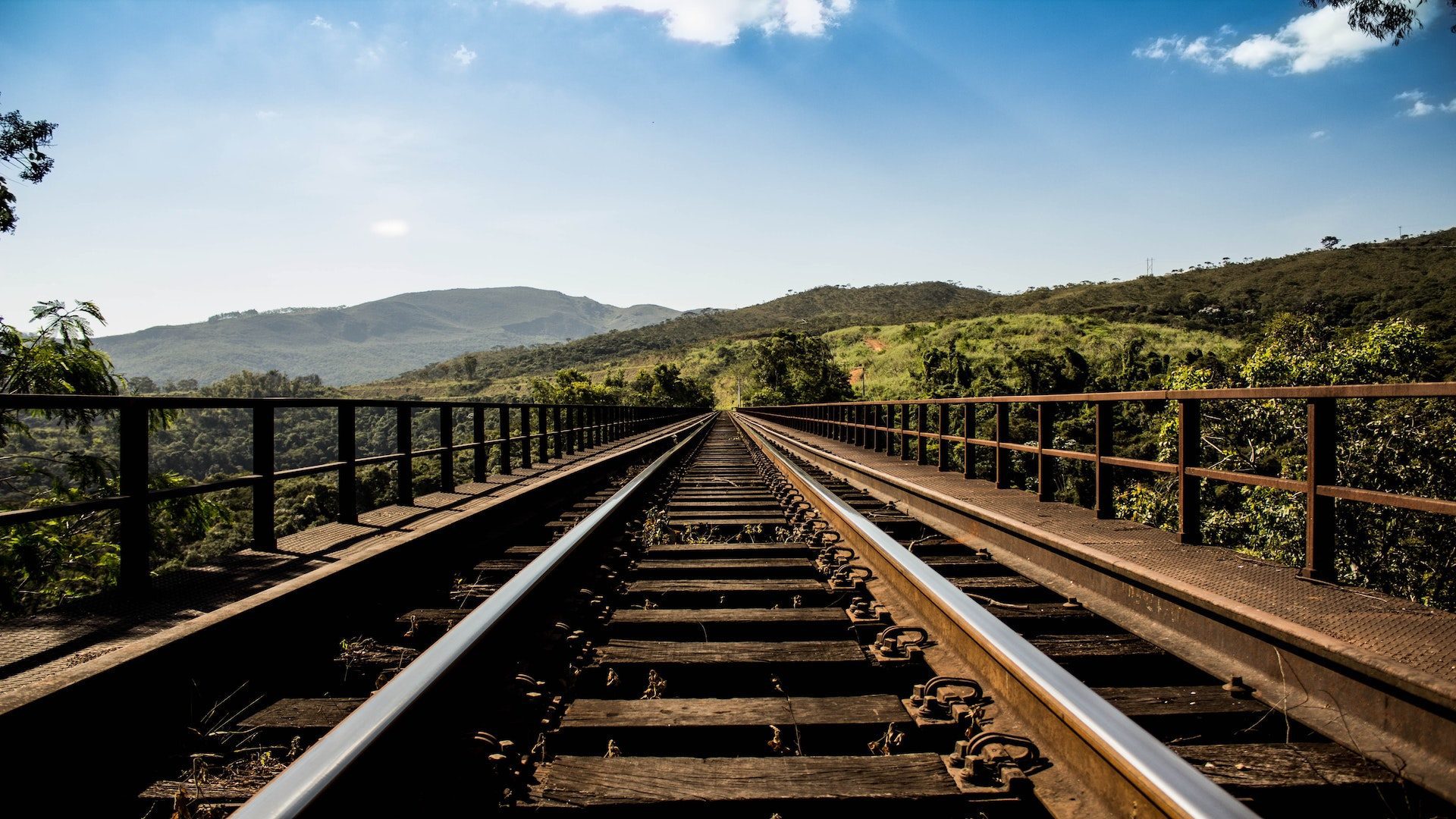 A railroad track leading off into the distance on a sunny day with blue skies and clouds.