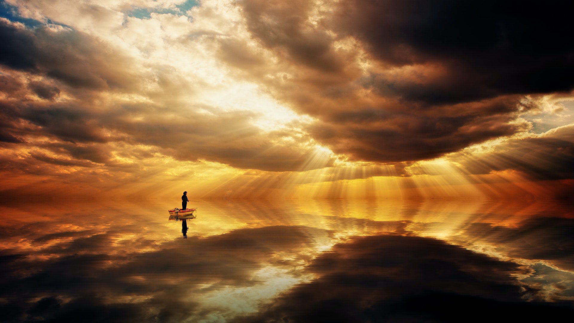 A reflective photo of a person standing in a small wooden boat out on the water at sunset.