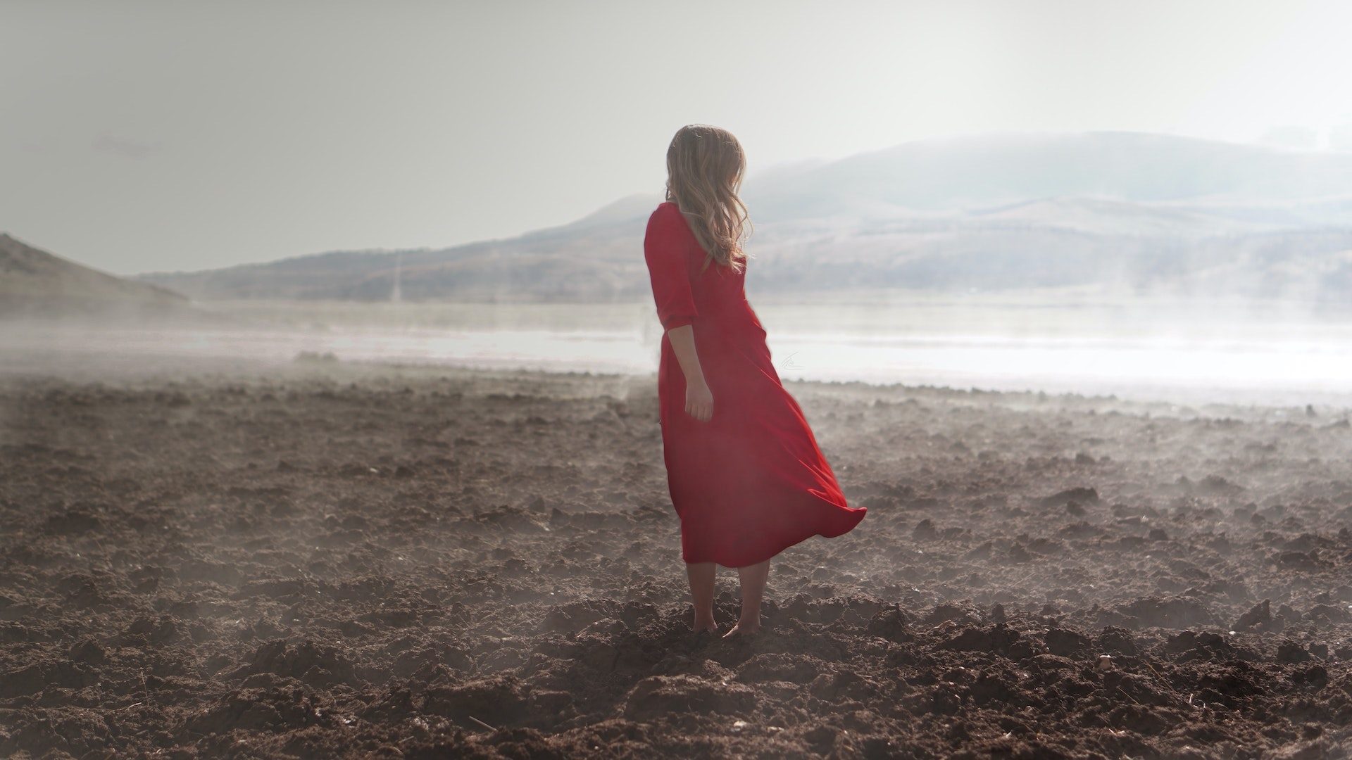 A woman in a red dress stands in a desolate desert.