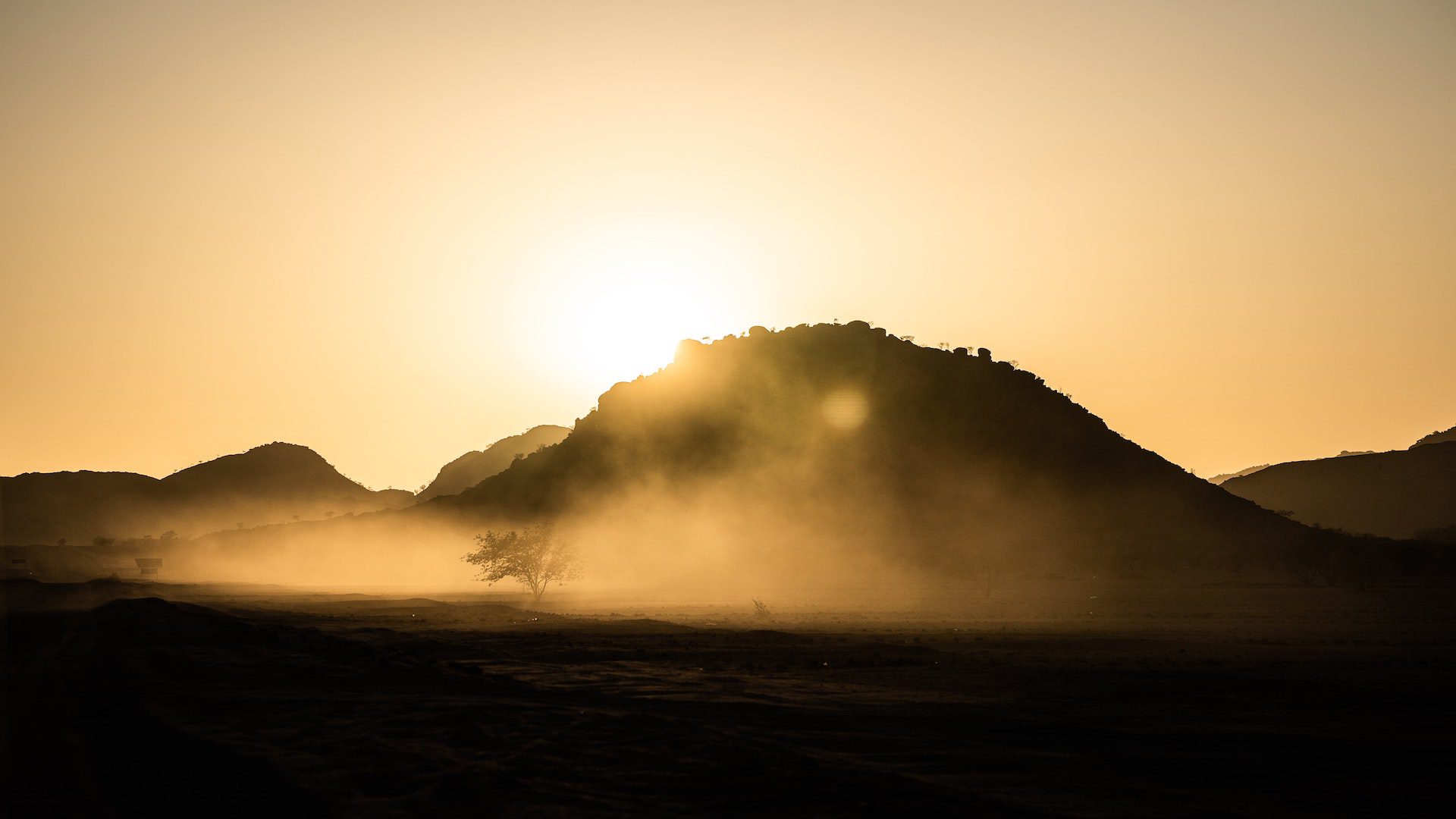 A silhouette of a mountain as the sun sets and the dust flys around.
