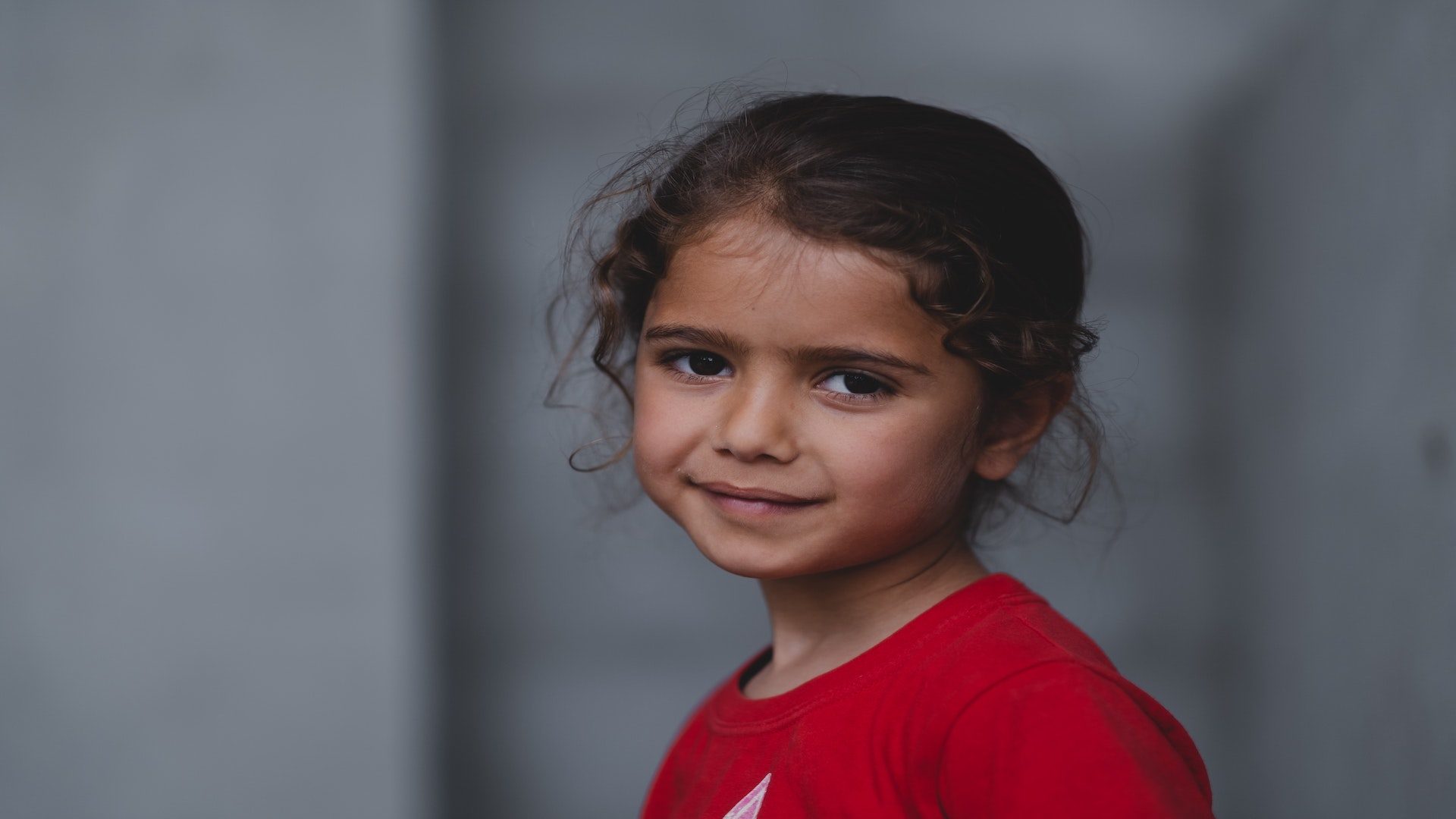 Picture of a young girl with curly hair and a red shirt.