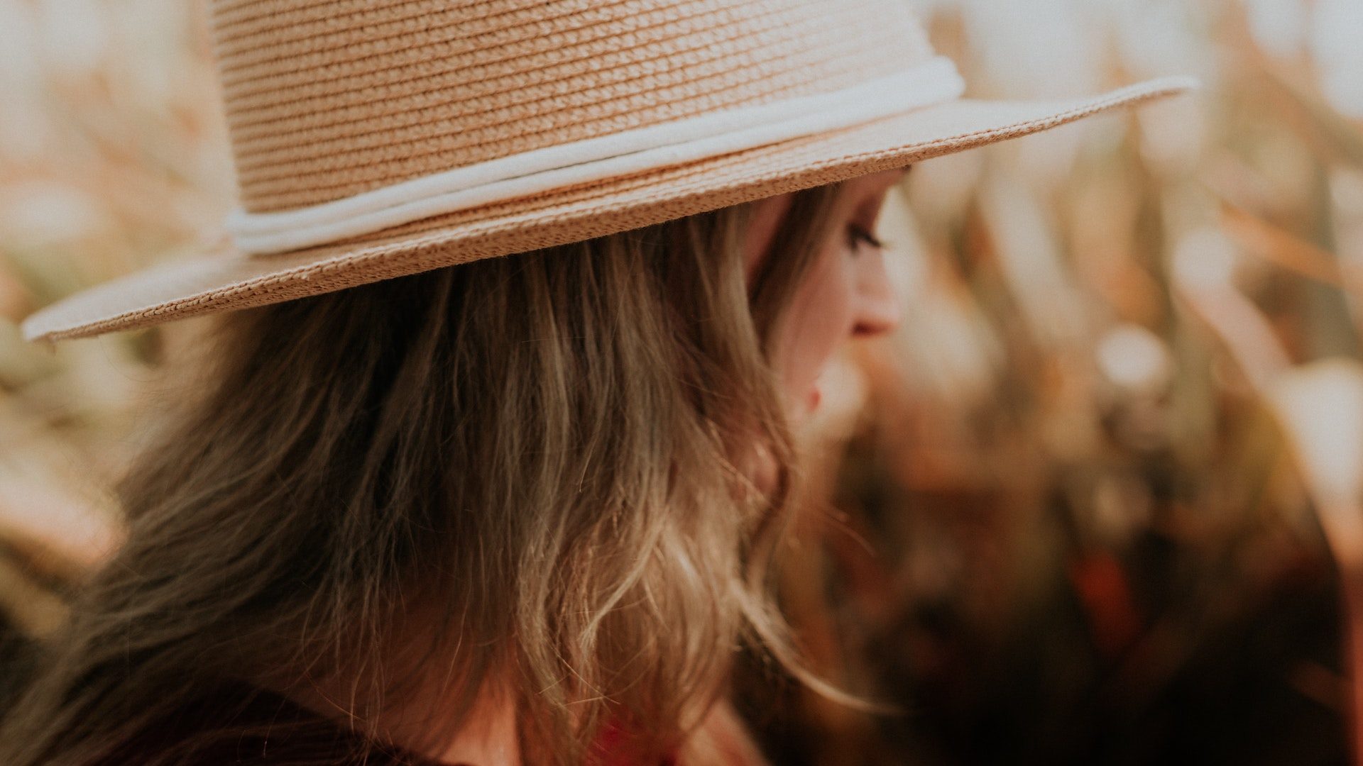 The side profile of a women with blonde hair who is wearing a tan hat in a field.