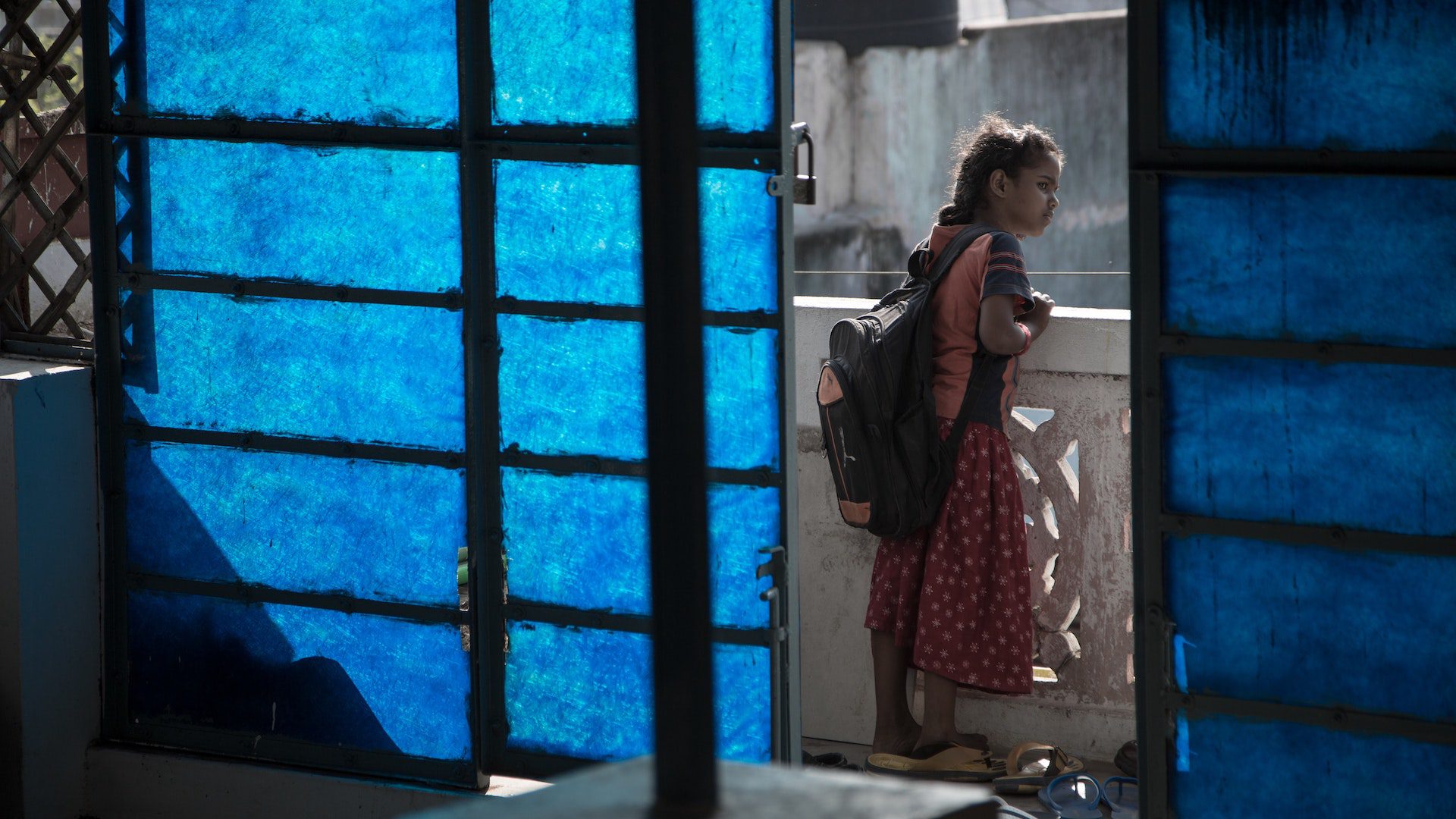 A young girl wearing a backpack is peering over the side of a balcony.