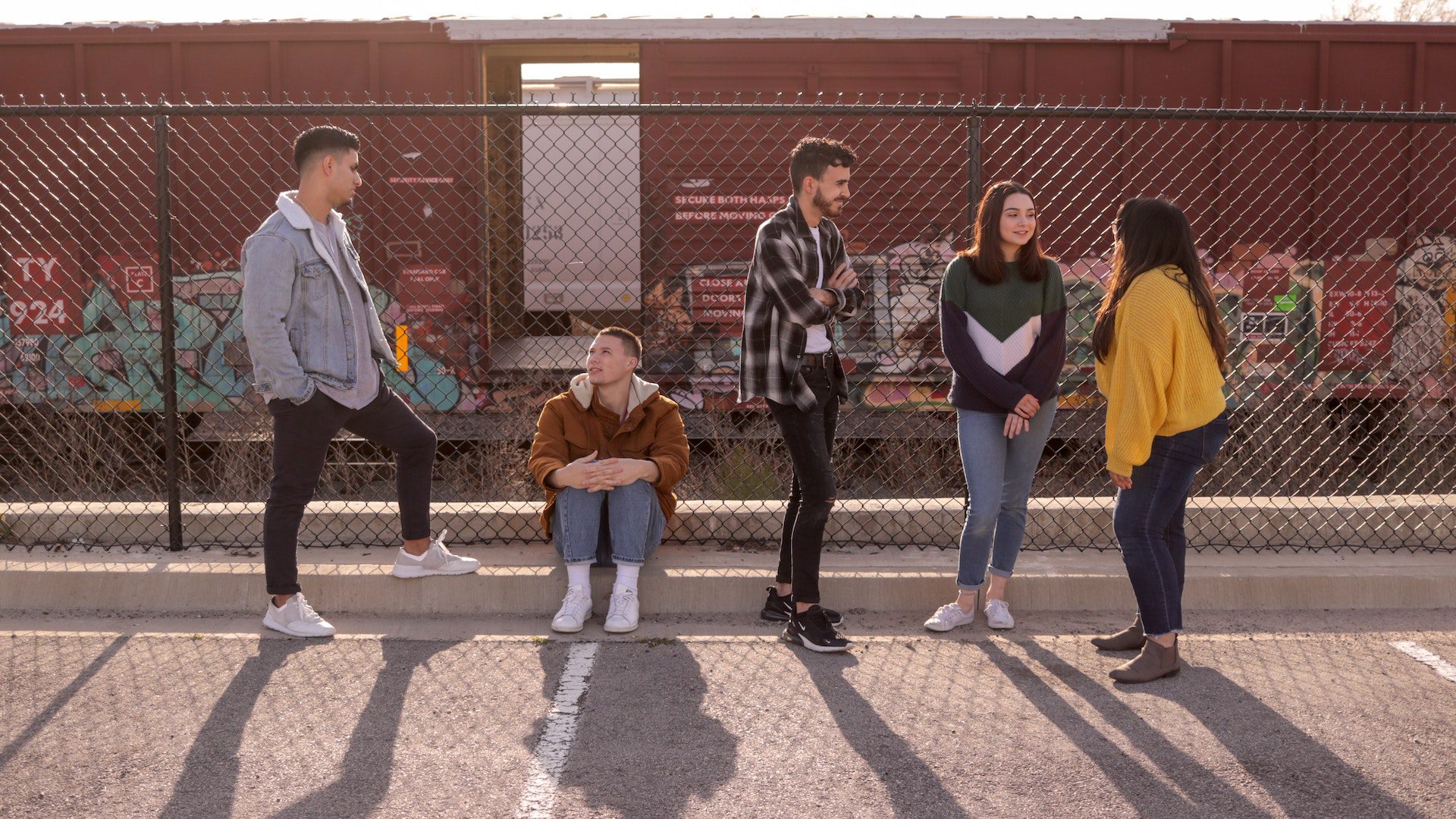 A group of people are talking in front of a chain linked fence and railroad track.