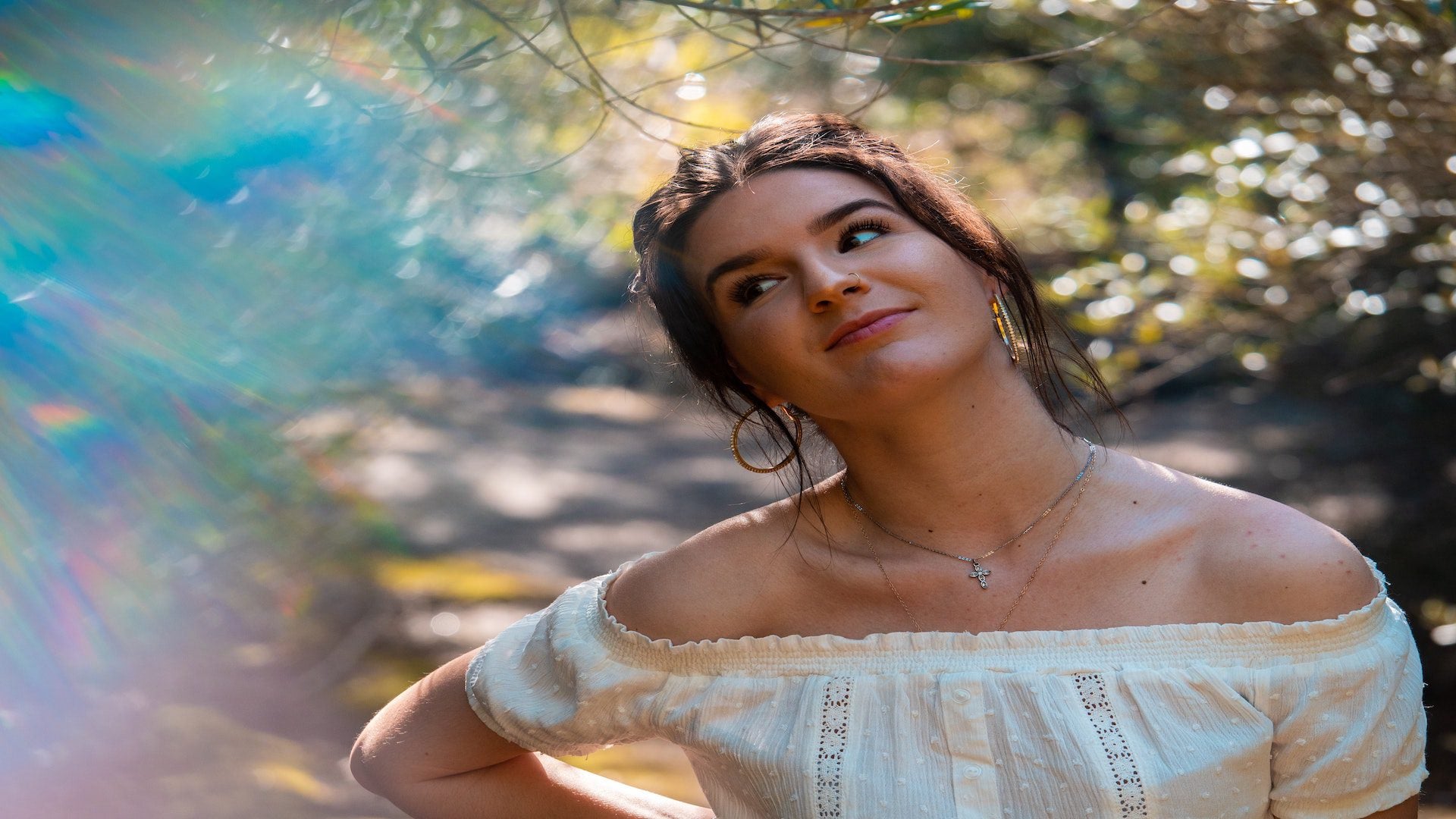A woman in a white blouse is standing under a tree with her face tilted.