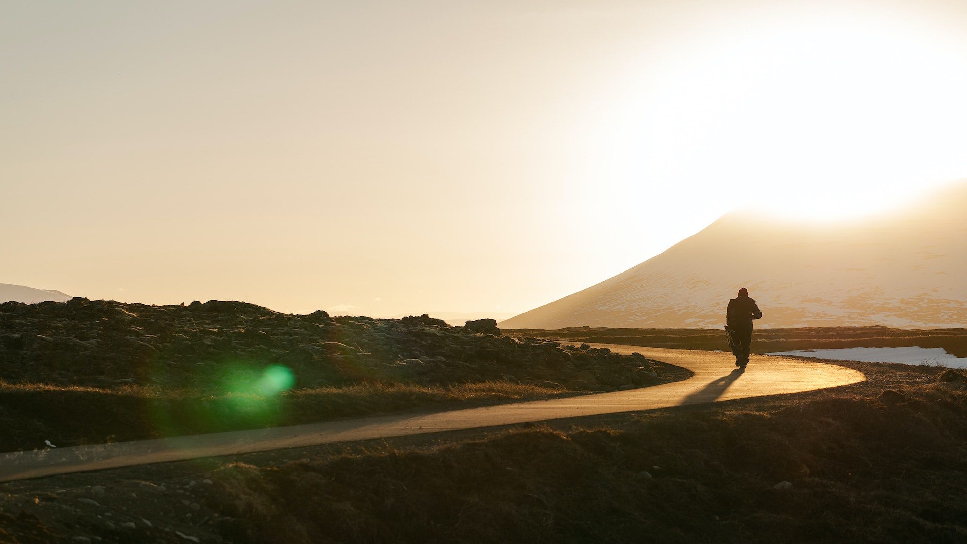 A person is walking on a winding road as the sun sets in the background.